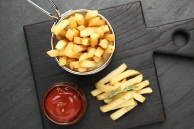 Photo of Tasty french fries served with ketchup and rosemary on black table, top view