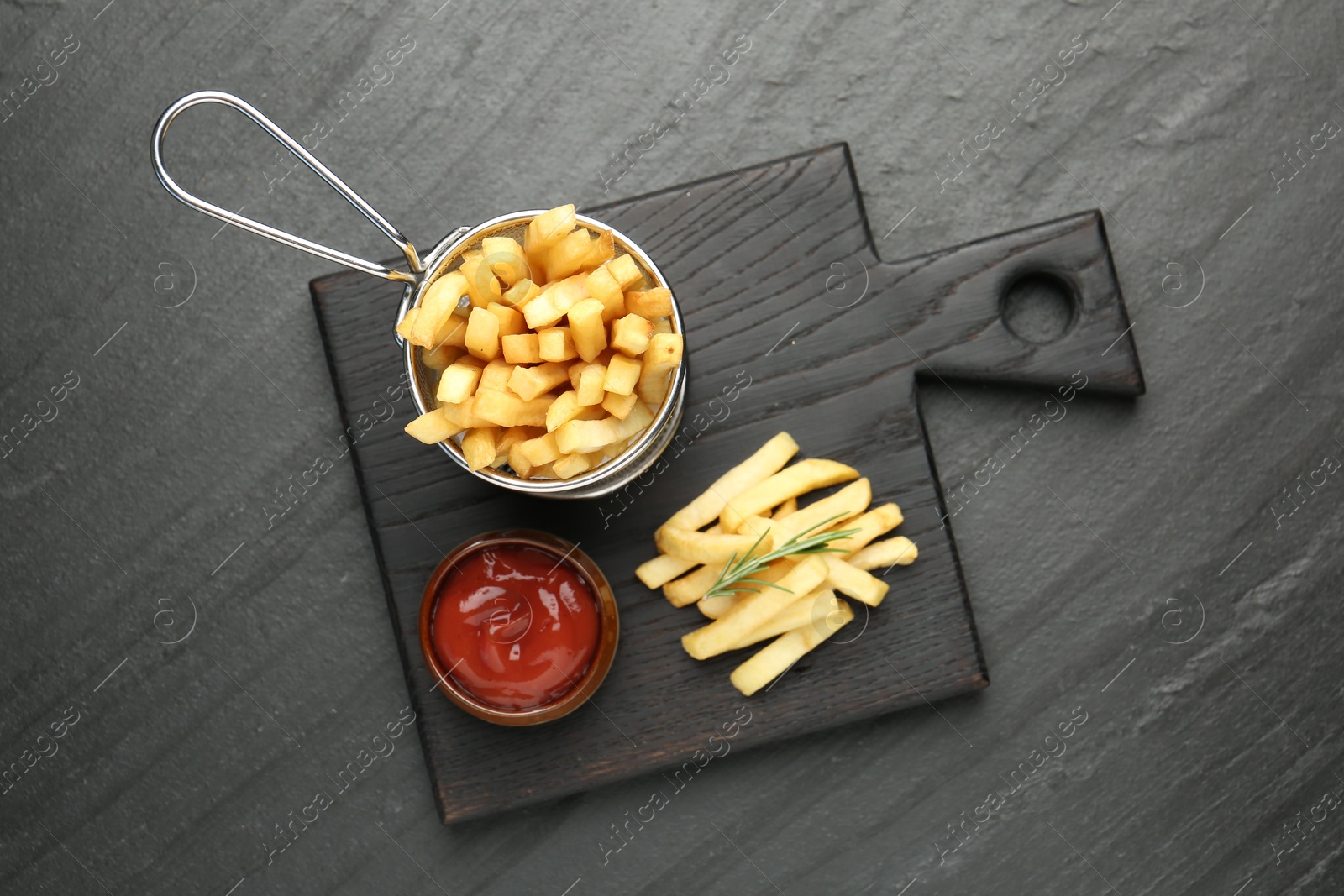 Photo of Tasty french fries served with ketchup and rosemary on black table, top view