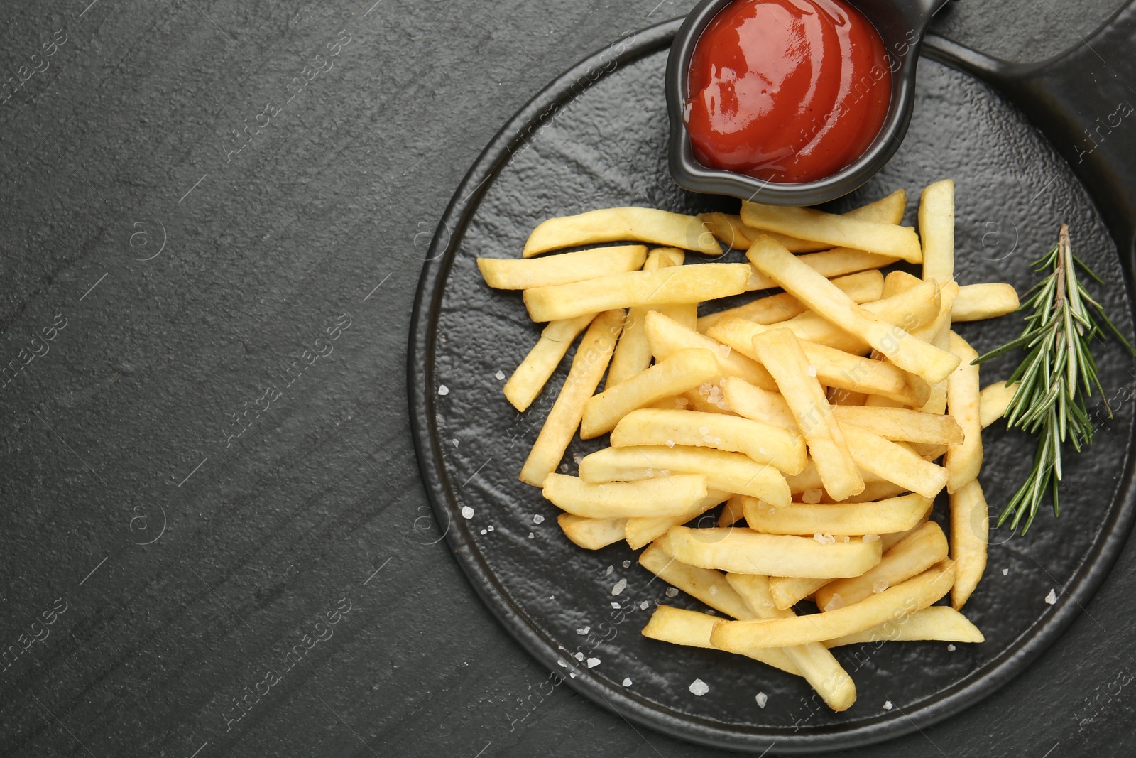 Photo of Tasty french fries served with ketchup and rosemary on black table, top view. Space for text