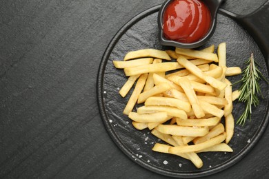 Photo of Tasty french fries served with ketchup and rosemary on black table, top view. Space for text