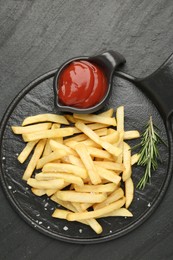 Photo of Tasty french fries served with ketchup and rosemary on black table, top view