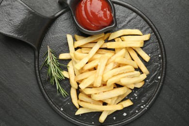 Photo of Tasty french fries served with ketchup and rosemary on black table, top view