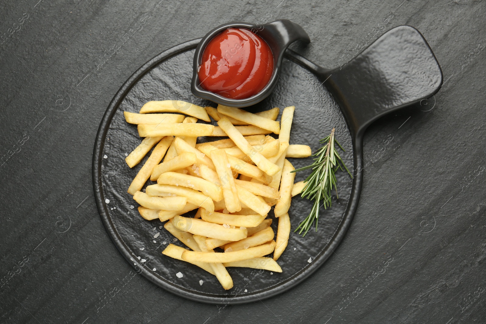 Tasty french fries served with ketchup and rosemary on black table, top view Photo of Tasty french fries served with ketchup and rosemary on black table, top view