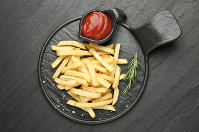Photo of Tasty french fries served with ketchup and rosemary on black table, top view