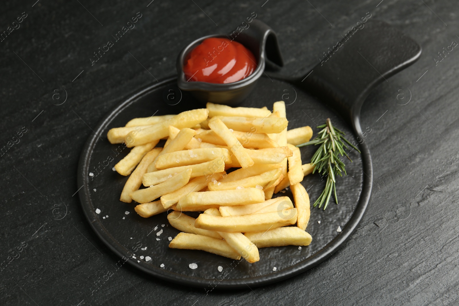 Photo of Tasty french fries served with ketchup and rosemary on black table, closeup