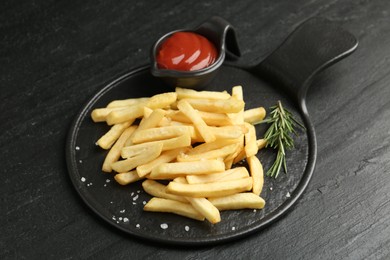 Photo of Tasty french fries served with ketchup and rosemary on black table, closeup