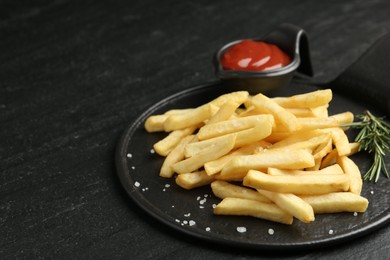 Photo of Tasty french fries served with ketchup and rosemary on black table, closeup. Space for text