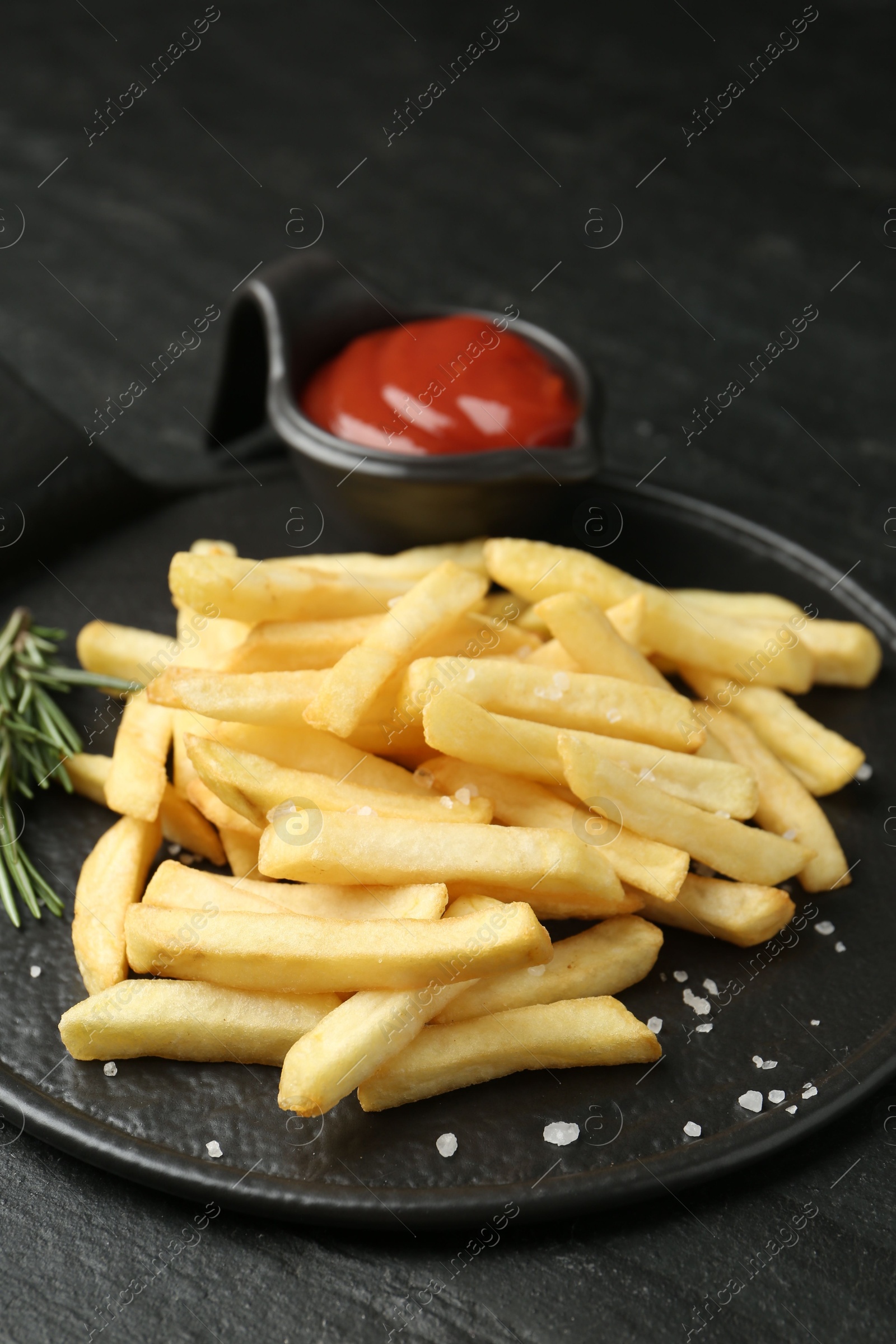 Photo of Tasty french fries served with ketchup and rosemary on black table, closeup