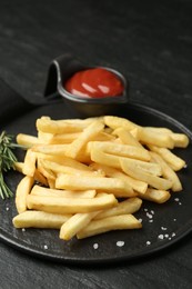 Photo of Tasty french fries served with ketchup and rosemary on black table, closeup