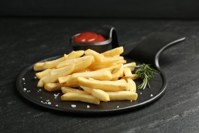 Photo of Tasty french fries served with ketchup and rosemary on black table, closeup