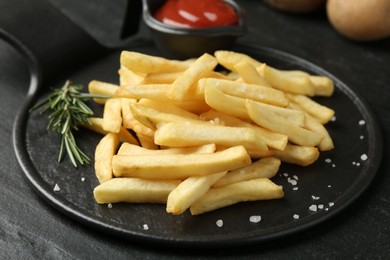 Photo of Tasty french fries served with ketchup and rosemary on black table, closeup
