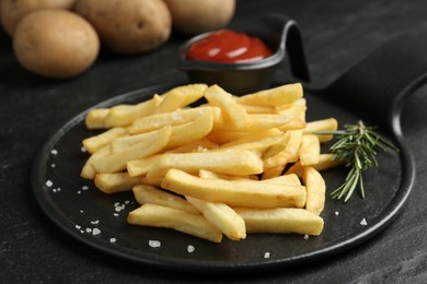 Photo of Tasty french fries served with ketchup and rosemary on black table, closeup