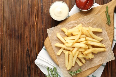 Photo of Tasty french fries served with sauces and rosemary on wooden table, flat lay. Space for text