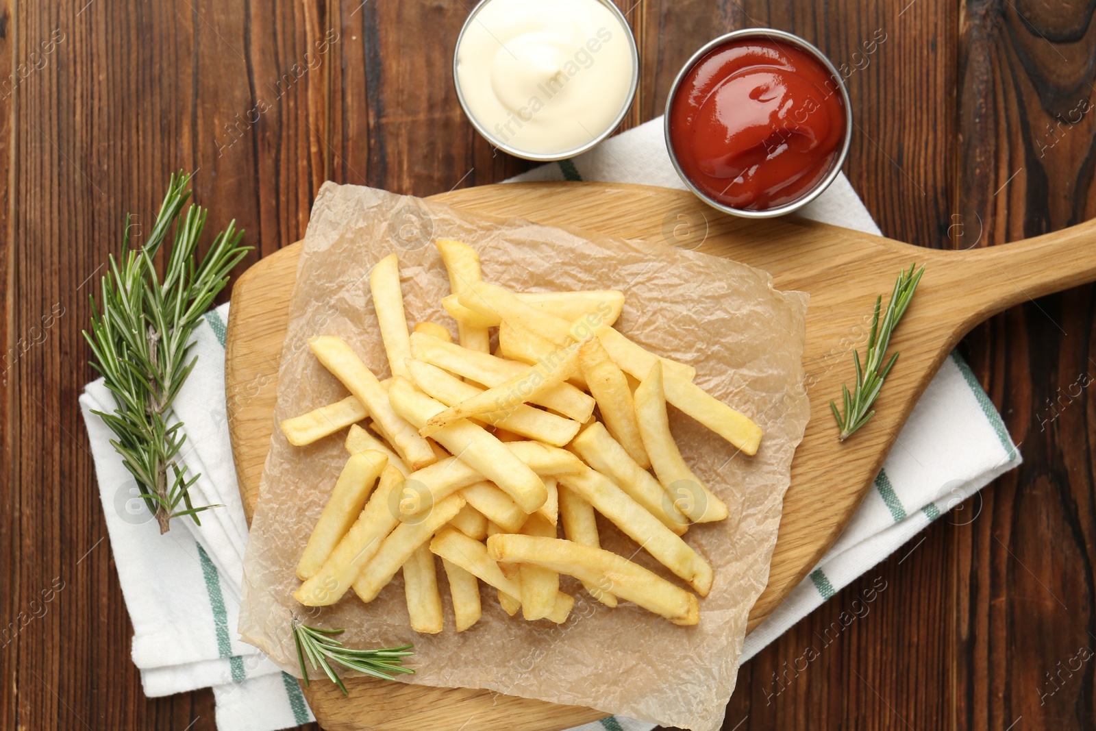 Tasty french fries served with sauces and rosemary on wooden table, flat lay Photo of Tasty french fries served with sauces and rosemary on wooden table, flat lay