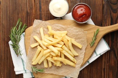 Photo of Tasty french fries served with sauces and rosemary on wooden table, flat lay