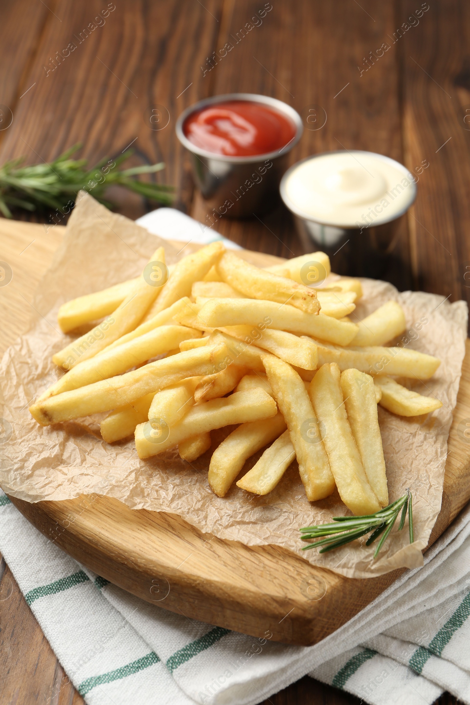 Tasty french fries served with sauces and rosemary on wooden table, closeup Photo of Tasty french fries served with sauces and rosemary on wooden table, closeup