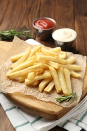 Photo of Tasty french fries served with sauces and rosemary on wooden table, closeup