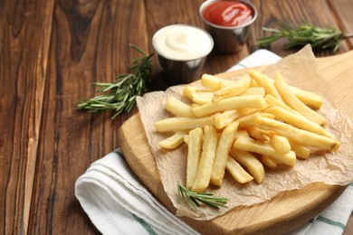 Photo of Tasty french fries served with sauces and rosemary on wooden table, closeup. Space for text