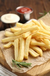 Photo of Tasty french fries served with sauces and rosemary on wooden table, closeup