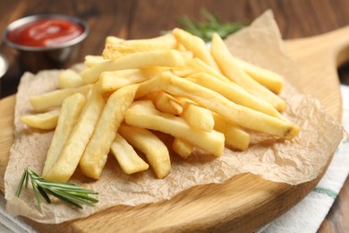Photo of Tasty french fries served with ketchup and rosemary on wooden table, closeup