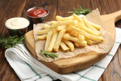 Photo of Tasty french fries served with sauces and rosemary on wooden table, closeup