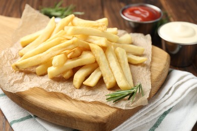 Photo of Tasty french fries served with sauces and rosemary on wooden table, closeup