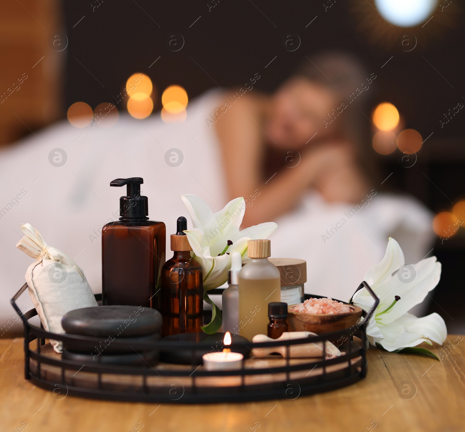 Senior woman relaxing on massage couch indoors, focus on different spa products and lily flowers Photo of Senior woman relaxing on massage couch indoors, focus on different spa products and lily flowers