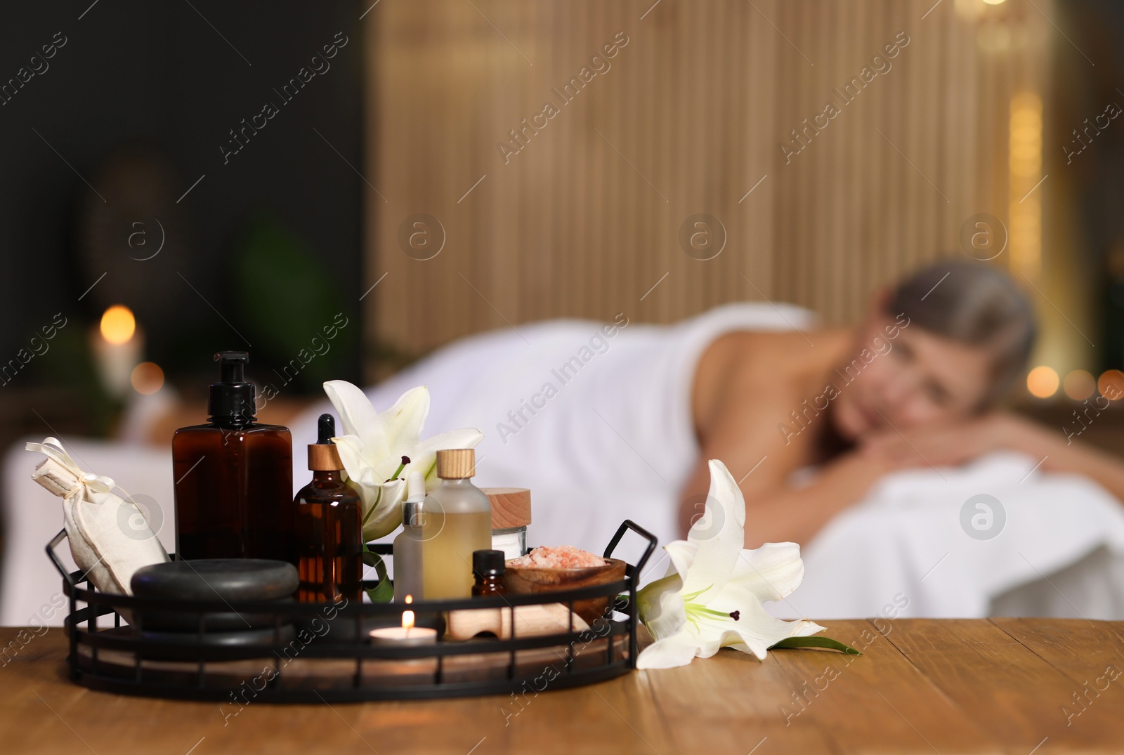 Senior woman relaxing on massage couch indoors, focus on different spa products and lily flowers Photo of Senior woman relaxing on massage couch indoors, focus on different spa products and lily flowers
