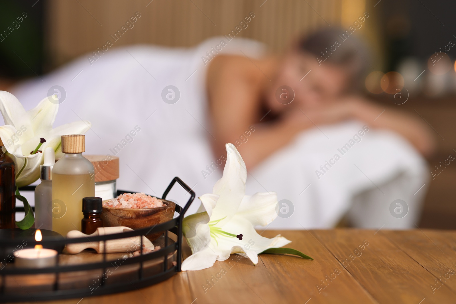 Senior woman relaxing on massage couch indoors, focus on different spa products and lily flowers Photo of Senior woman relaxing on massage couch indoors, focus on different spa products and lily flowers