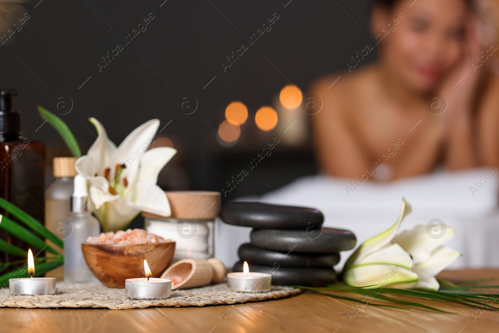 Beautiful woman relaxing on massage couch indoors, focus on different spa products and lily flowers Photo of Beautiful woman relaxing on massage couch indoors, focus on different spa products and lily flowers