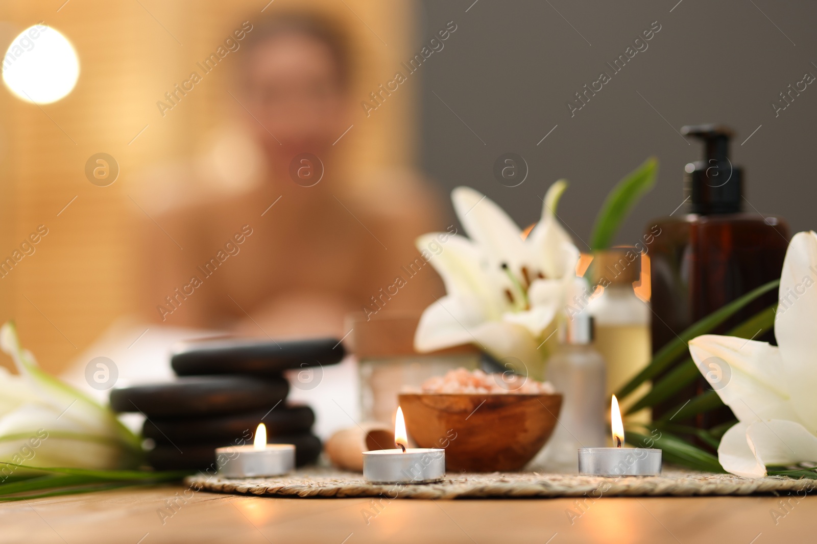 Beautiful woman relaxing on massage couch indoors, focus on different spa products and lily flowers Photo of Beautiful woman relaxing on massage couch indoors, focus on different spa products and lily flowers
