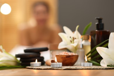 Photo of Beautiful woman relaxing on massage couch indoors, focus on different spa products and lily flowers