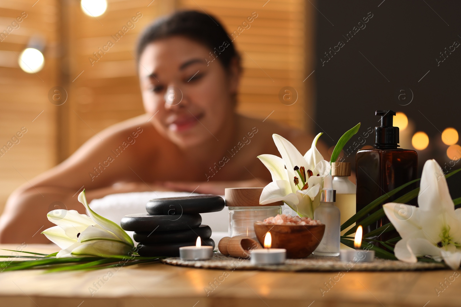 Beautiful woman relaxing on massage couch indoors, focus on different spa products and lily flowers Photo of Beautiful woman relaxing on massage couch indoors, focus on different spa products and lily flowers