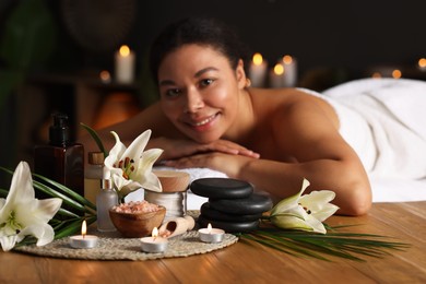 Photo of Beautiful woman relaxing on massage couch indoors, focus on different spa products and lily flowers