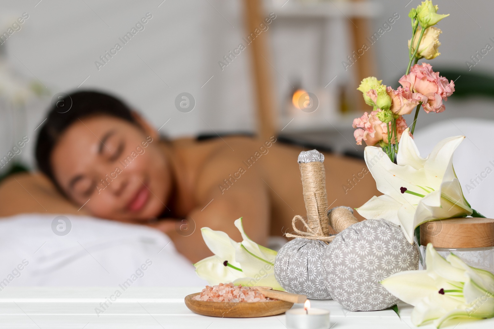 Beautiful woman relaxing on massage couch indoors, focus on different spa products and lily flowers Photo of Beautiful woman relaxing on massage couch indoors, focus on different spa products and lily flowers