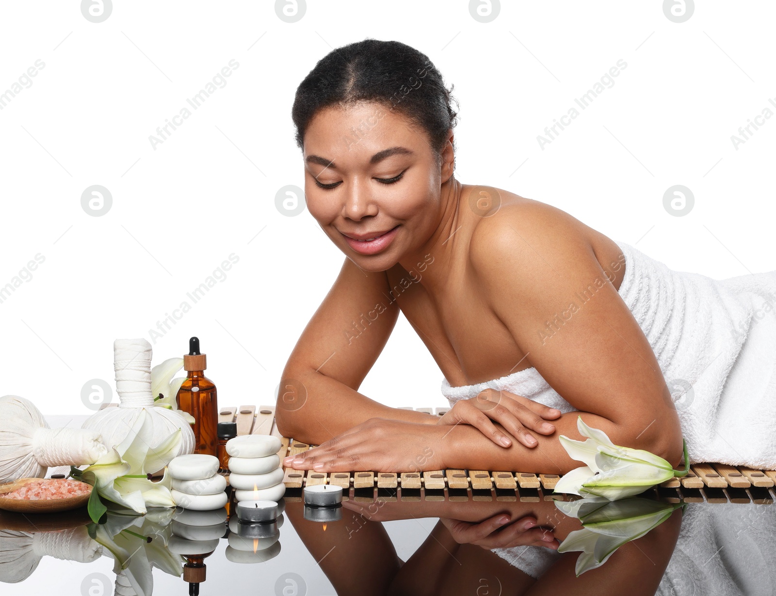 Photo of Beautiful woman relaxing on bamboo mat against white background. Different spa products and lily flowers on mirror surface