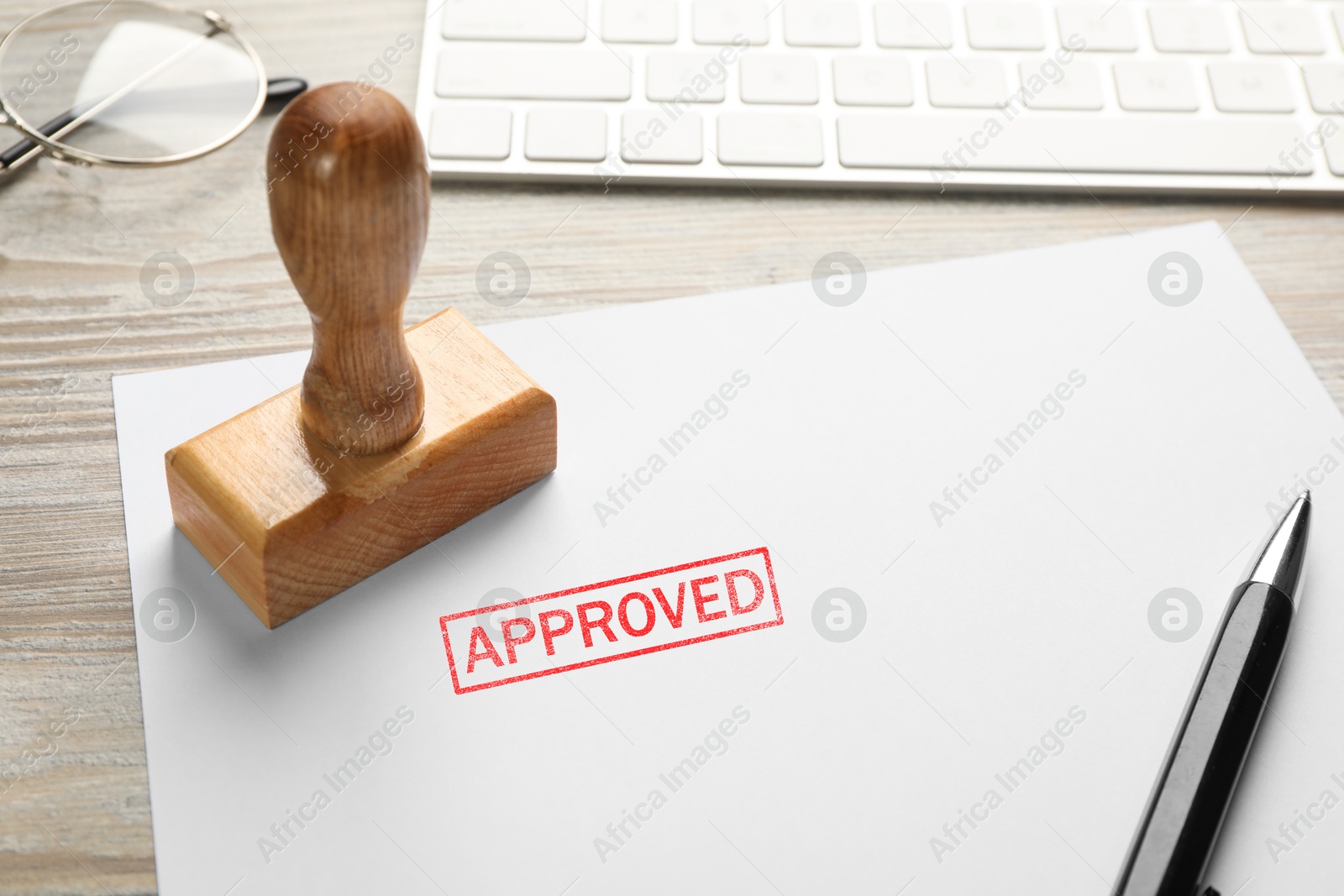 Sheet of paper with word Approved, stamp, keyboard and pen on white wooden table, closeup Image of Sheet of paper with word Approved, stamp, keyboard and pen on white wooden table, closeup