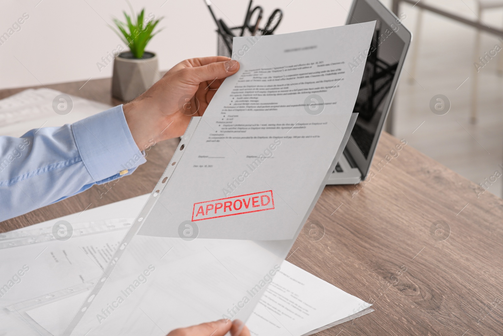 Man holding document with Approved stamp at wooden table in office, closeup Image of Man holding document with Approved stamp at wooden table in office, closeup