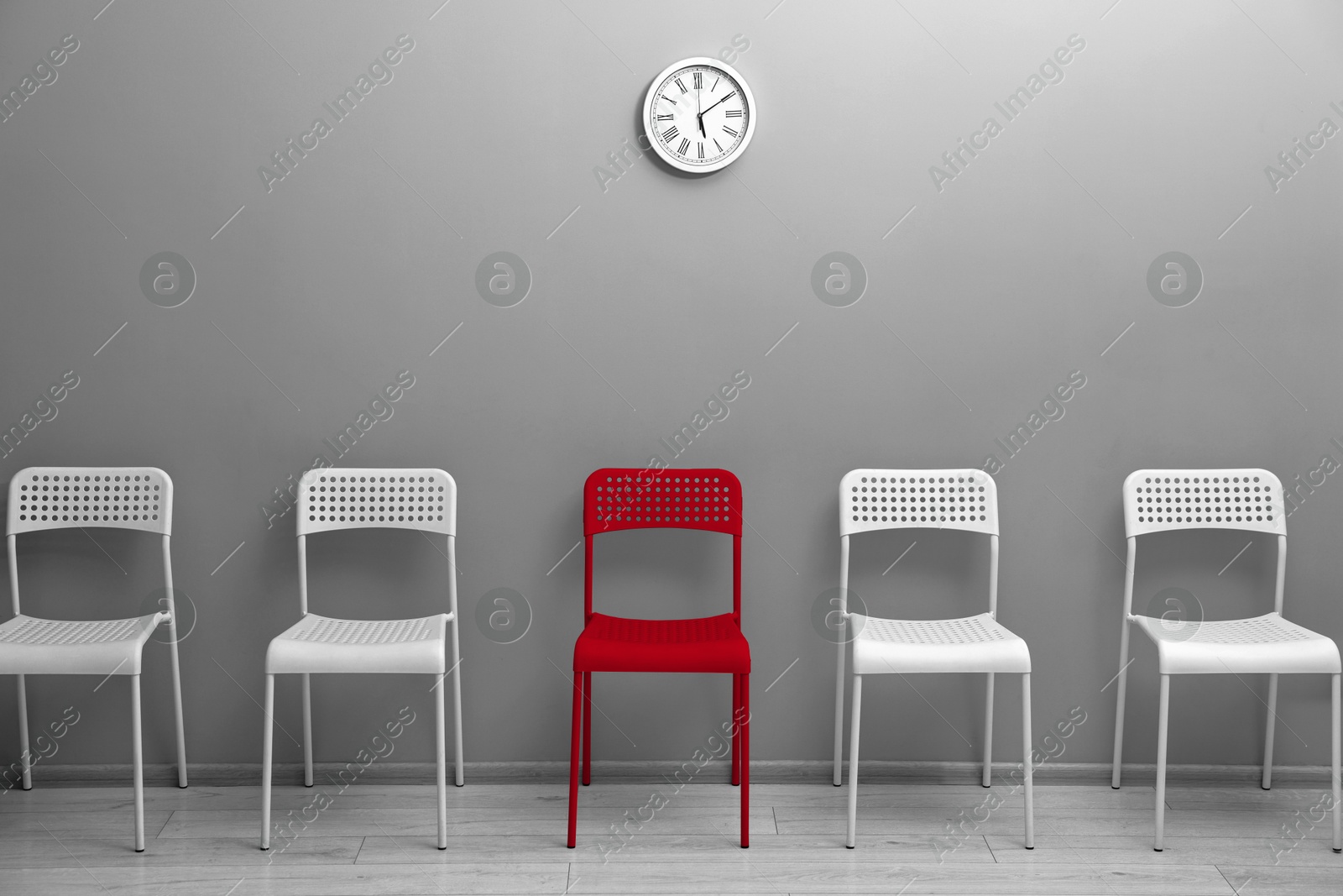Image of Different, unique, special. Red chair among white ones near grey wall indoors