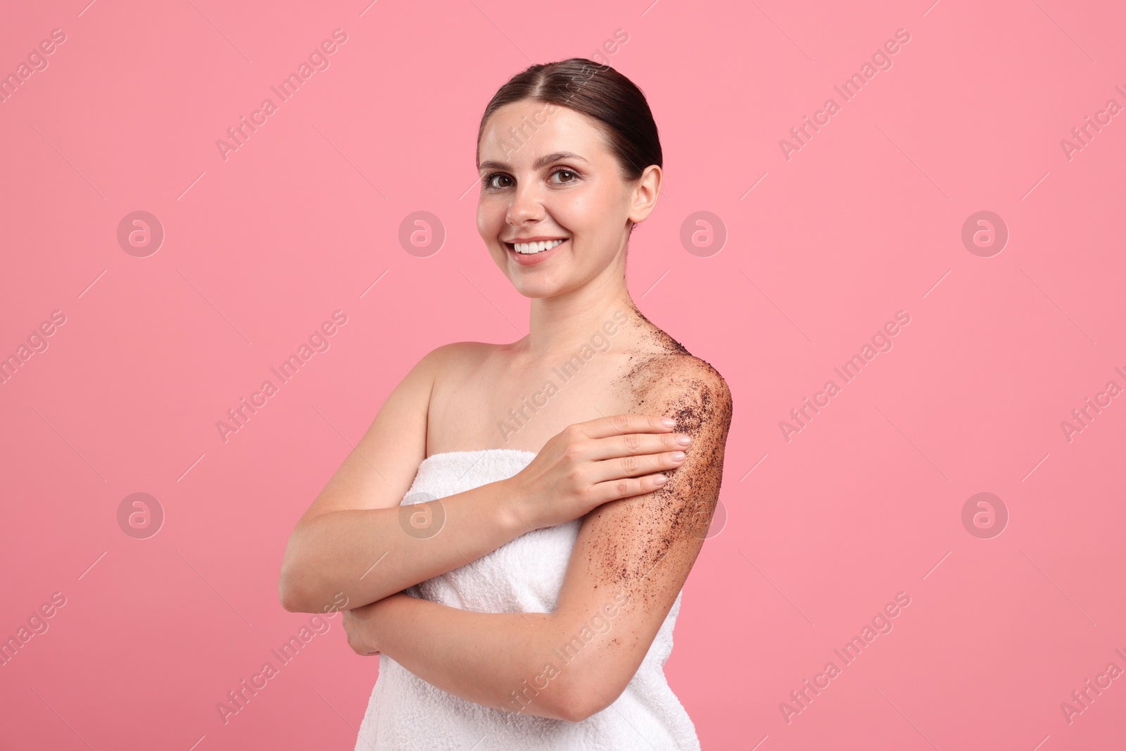 Smiling woman applying body scrub onto her arm against pink background Photo of Smiling woman applying body scrub onto her arm against pink background