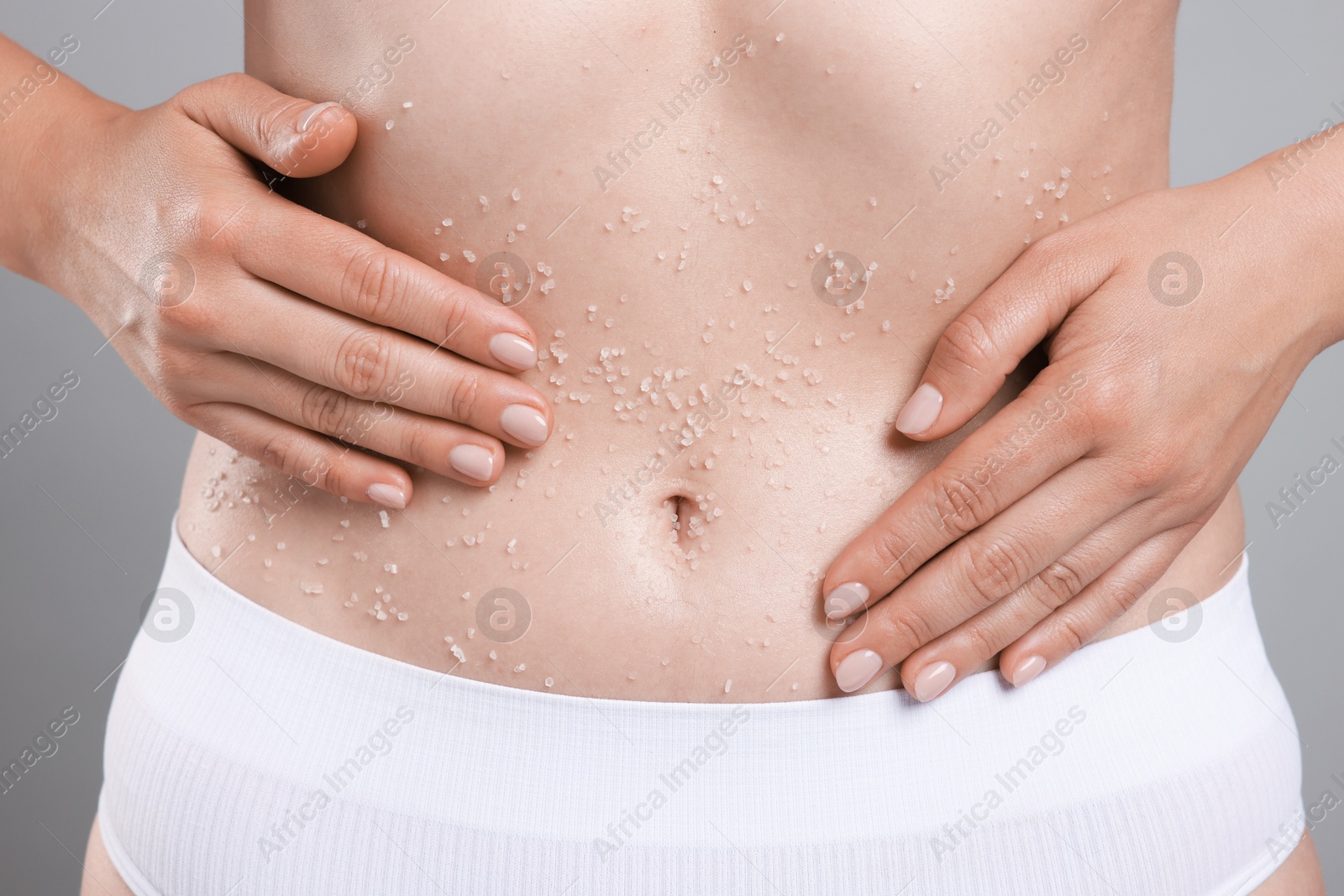 Woman applying body scrub onto her belly against grey background, closeup Photo of Woman applying body scrub onto her belly against grey background, closeup