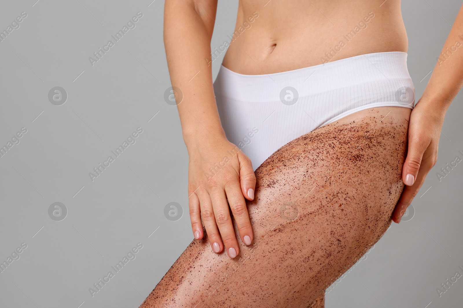 Woman with body scrub on her leg against grey background, closeup. Space for text Photo of Woman with body scrub on her leg against grey background, closeup. Space for text