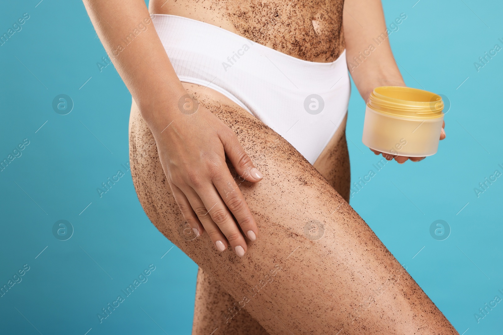 Photo of Woman with body scrub on her skin and jar against light blue background, closeup