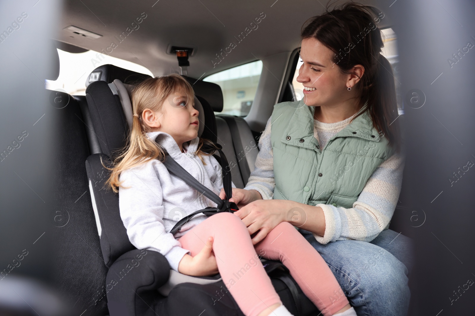 Happy mother fastening her daughter in child safety seat inside car Photo of Happy mother fastening her daughter in child safety seat inside car