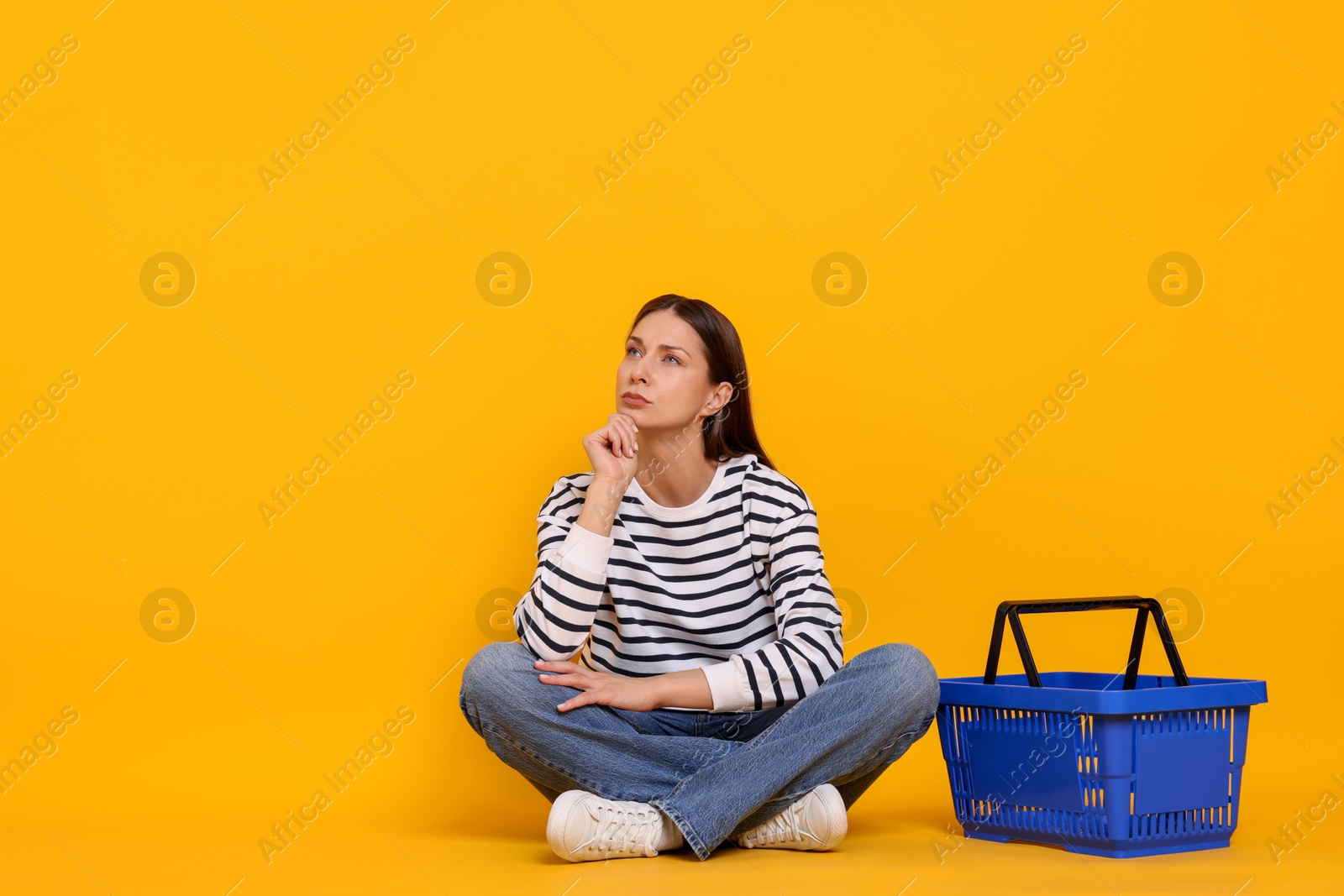 Photo of Thoughtful woman with shopping basket on yellow background. Space for text