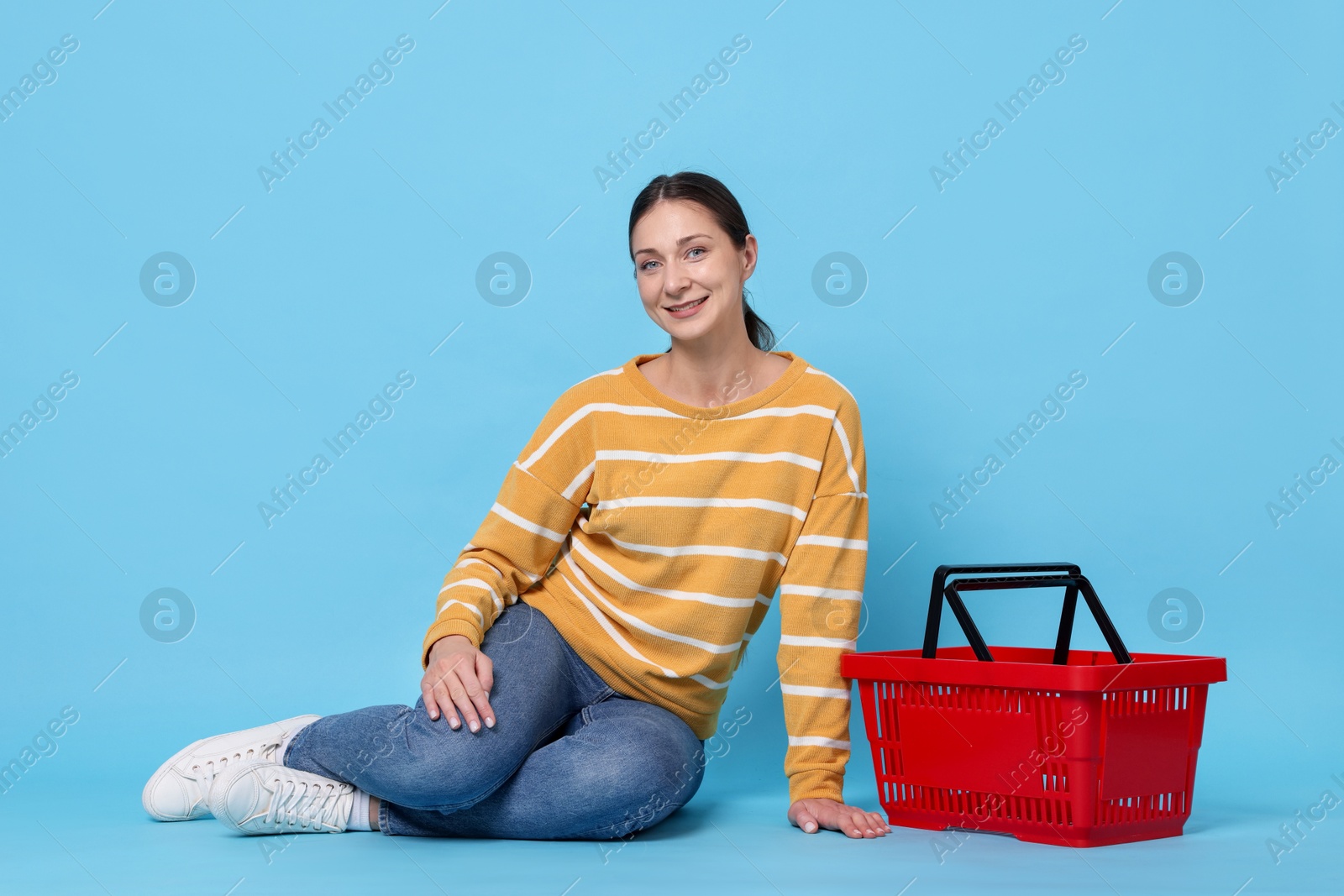 Photo of Smiling woman and shopping basket on light blue background