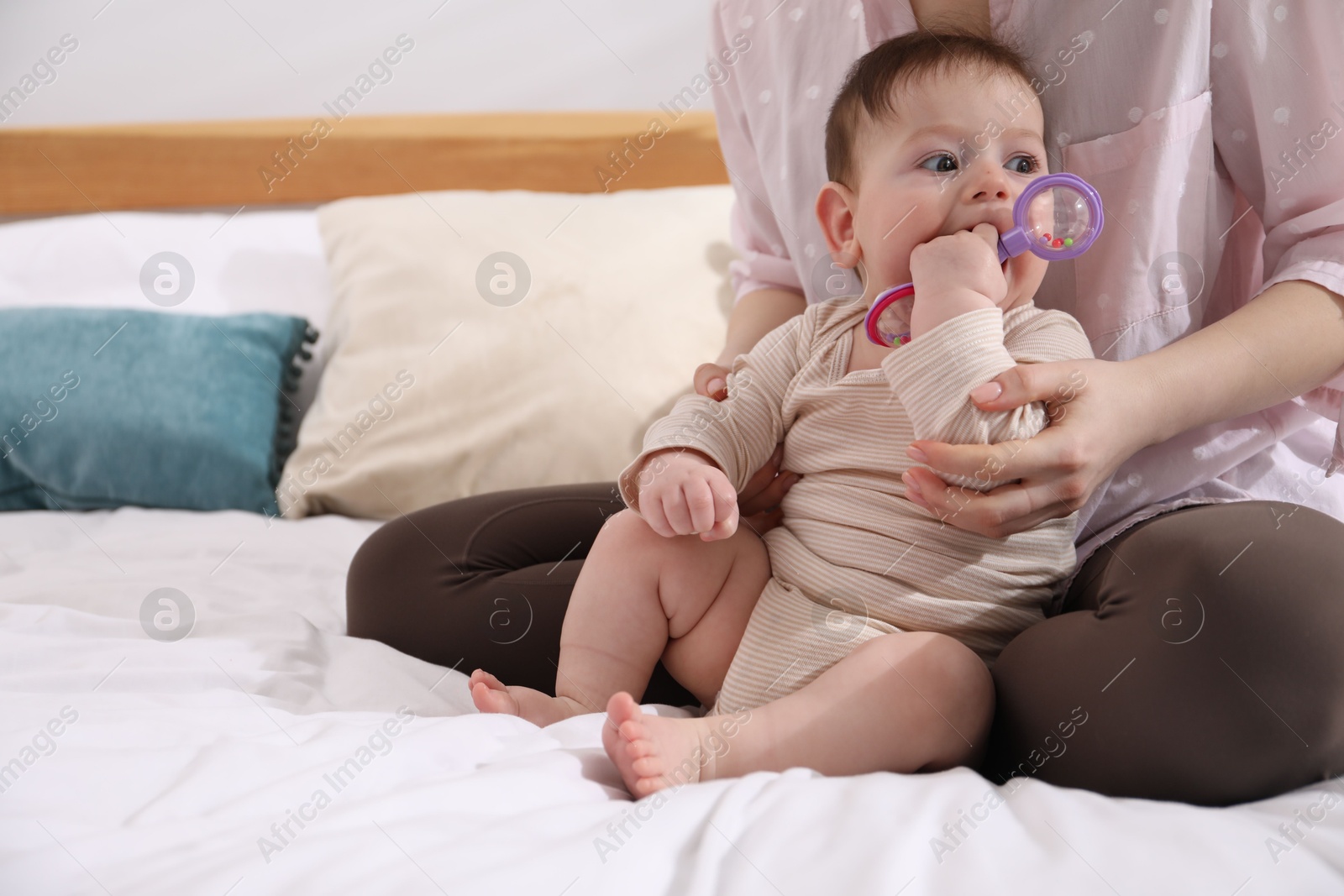 Mother and her cute little baby with rattle toy on bed at home, closeup. Space for text Photo of Mother and her cute little baby with rattle toy on bed at home, closeup. Space for text