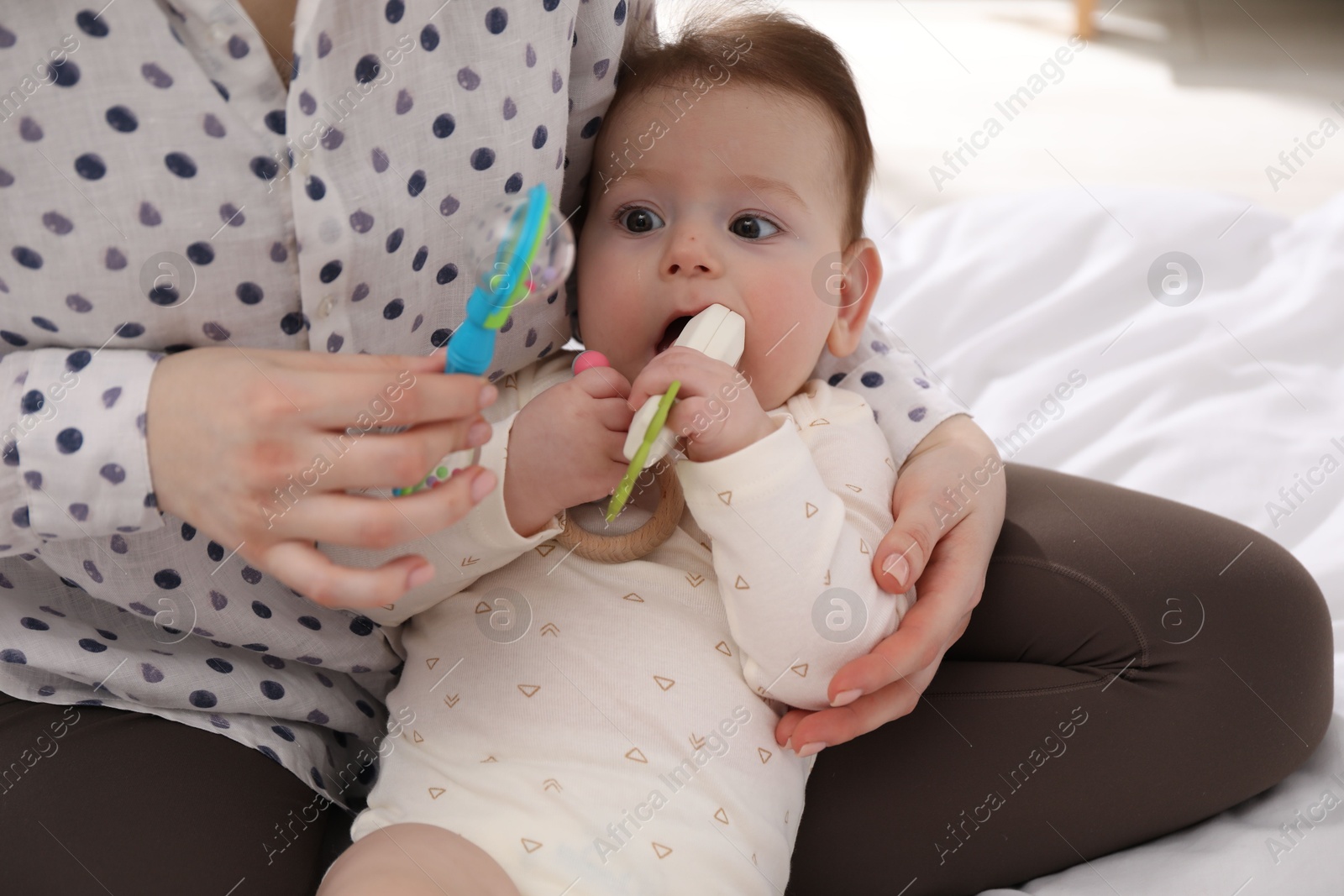 Mother and her cute little baby with rattle toy on bed at home, closeup Photo of Mother and her cute little baby with rattle toy on bed at home, closeup