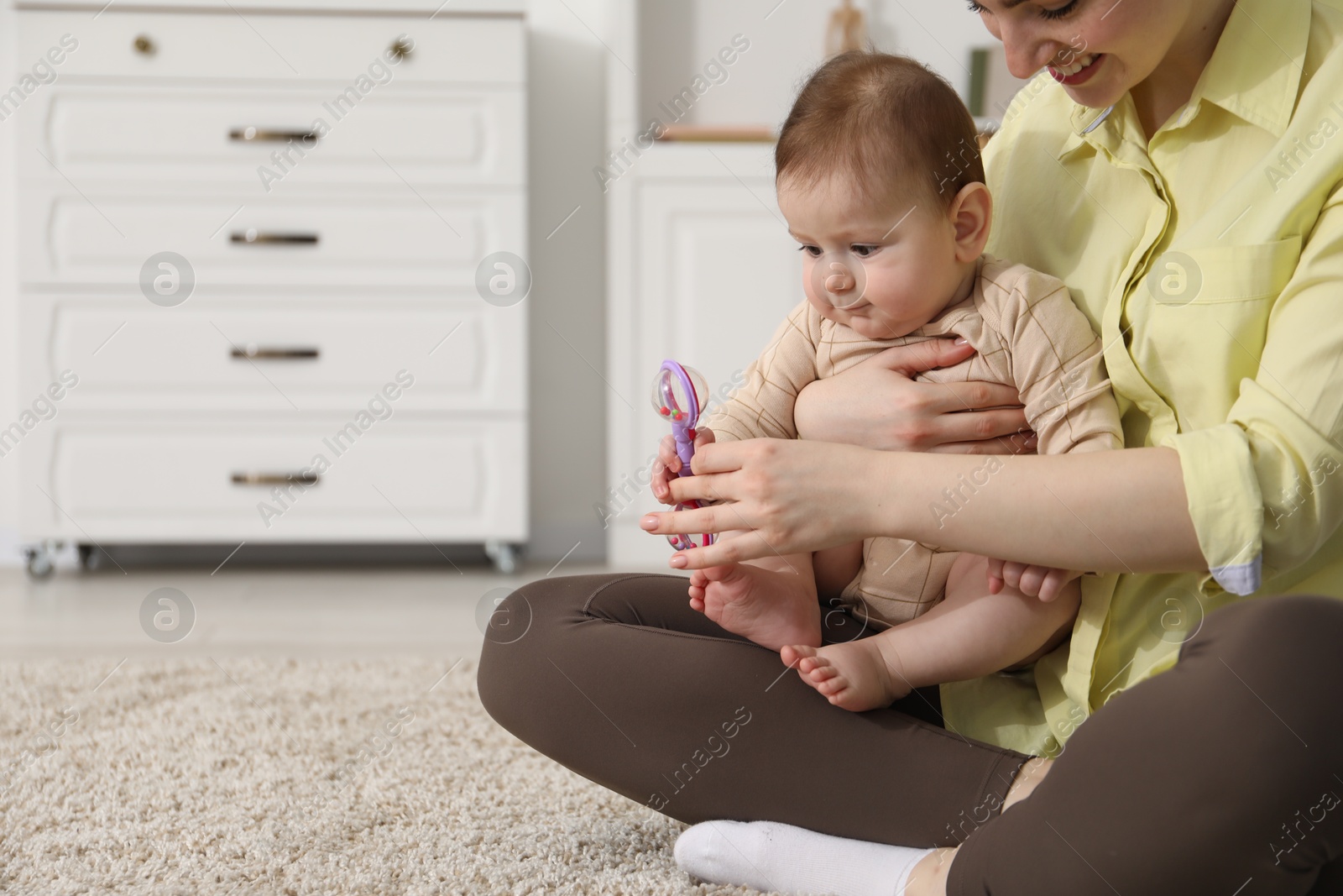 Mother and her cute little baby with rattle toy on floor at home, closeup. Space for text Photo of Mother and her cute little baby with rattle toy on floor at home, closeup. Space for text