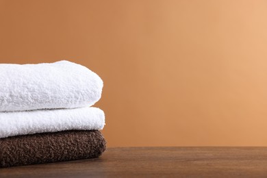 Photo of Stack of clean towels on wooden table against brown background, space for text